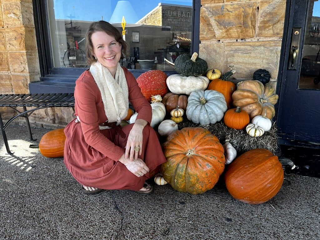 The owner of A Pumpkin Story beside a storefront display of heirloom pumpkins
