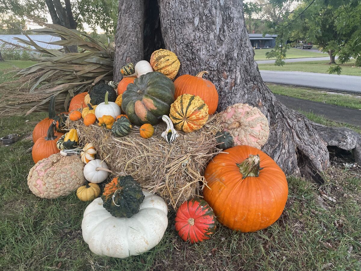 Stacked pumpkins and straw bales arranged along a porch rail